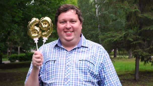 Великий чоловік тримає золоті кулі, що робить 69 номер відкритим. 69-річчя святкування вечірки — стокове відео