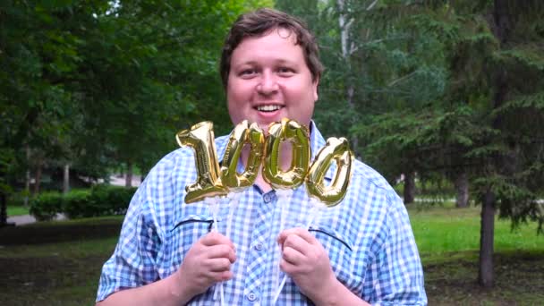 Grande homem segurando balões dourados fazendo o 1000 número ao ar livre. Festa de celebração do 0o aniversário — Vídeo de Stock