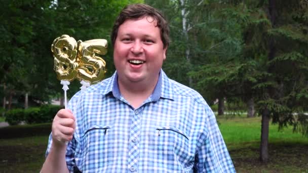 Big man innehar gyllene ballonger gör 85 nummer utomhus. 85-års jubileum fest — Stockvideo