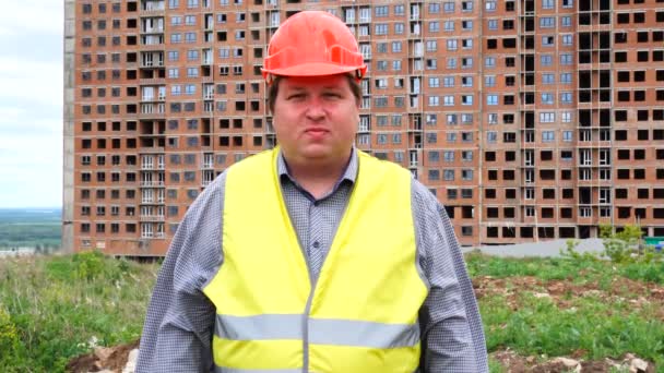 Mężczyzna budowniczy, pracownik lub architekt pracujący na budowie budynku stoi patrząc na kamerę — Wideo stockowe