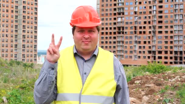 Hombre capataz constructor, trabajador o arquitecto en el sitio de construcción mostrando signo de victoria mientras sonríe a la cámara — Vídeos de Stock