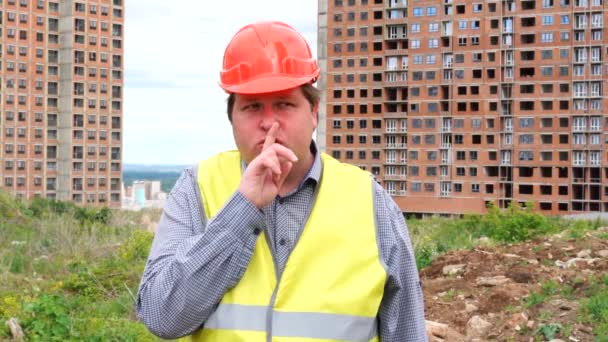 彼は沈黙を求める彼の唇に指を上げる静かなジェスチャーを作る建設建設現場のビルダー — ストック動画