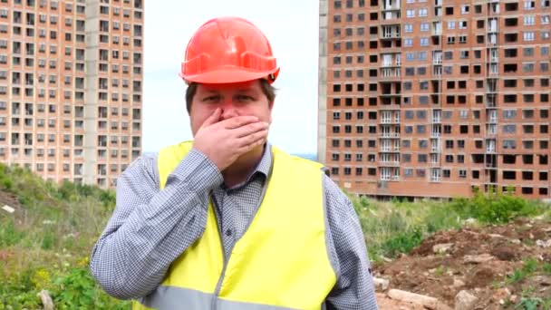 Joven constructor guapo hombre cubriendo la boca en el sitio de construcción — Vídeo de stock