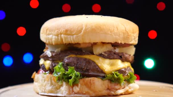 Chladný nádherný čerstvý šťavnatý Burger se otáčí na otočný stůl na pozadí barevných rozmazlných světel. — Stock video