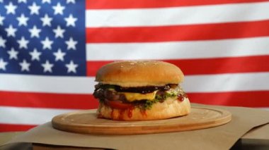 Burger, bir sığır eti, peynir ve sebze ile ABD bayrağının arka planında ahşap bir tahta üzerinde döner