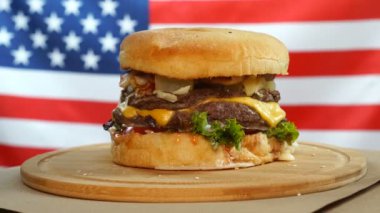 Burger, bir sığır eti, peynir ve sebze ile ABD bayrağının arka planında ahşap bir tahta üzerinde döner