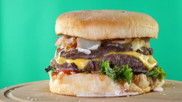 Burger, με βοδινό, τυρί και λαχανικά περιστρέφεται σε ένα ξύλινο Συμβούλιο. φόντο κλειδιού αποχρώσεων — Αρχείο Βίντεο