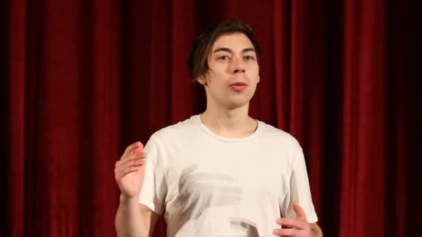 Młody mężczyzna wyjaśnia czerwone tło kurtyny — Wideo stockowe