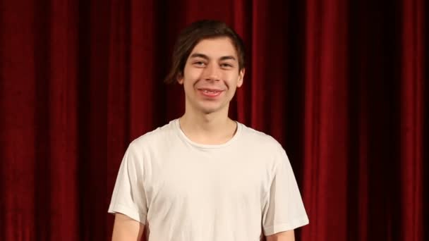 Joven hombre feliz sonriendo sobre fondo de cortina roja — Vídeo de stock