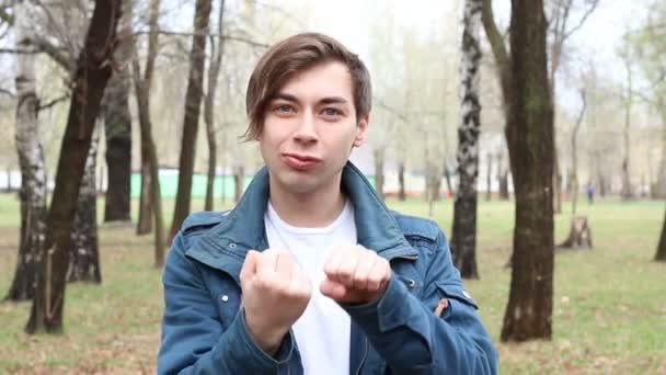 Retrato de joven caucásico guapo mostrando el dedo medio en el parque — Vídeos de Stock