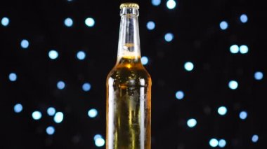Bira şişesi yakın çekim. Şişedeki hafif bira siyah arka plan üzerinde döndürülür.