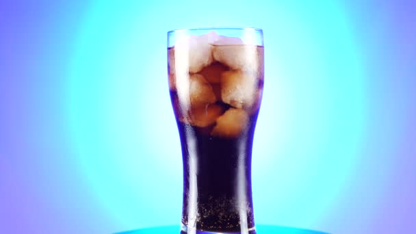Ein Glas Cola dreht sich langsam um die eigene Achse. Nahaufnahme 4k Video. blauer Hintergrund. — Stockvideo