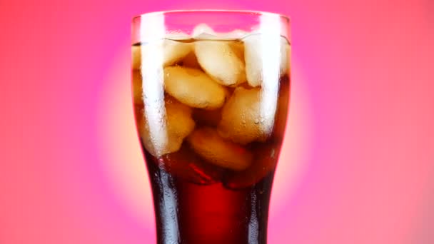 Ein Glas Cola dreht sich langsam um die eigene Achse. Nahaufnahme 4k Video. rosa Hintergrund. — Stockvideo