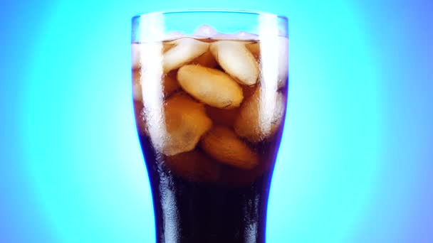 Glas cola draait langzaam rond zijn as. Close-up 4k-video. Blauwe achtergrond. — Stockvideo
