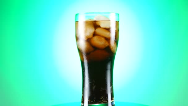 Glass of cola turns slowly around its axis. Close up 4K video. Green background. — Stock Video