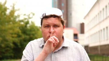 Müslüman adam sessizlik isterken baştan çıkarıcı bir jestle parmağını dudaklarına doğru kaldırarak suskun bir jest yapıyor.