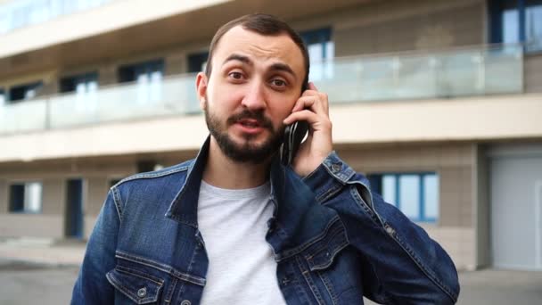 Guapo joven con barba está hablando por teléfono al aire libre — Vídeos de Stock