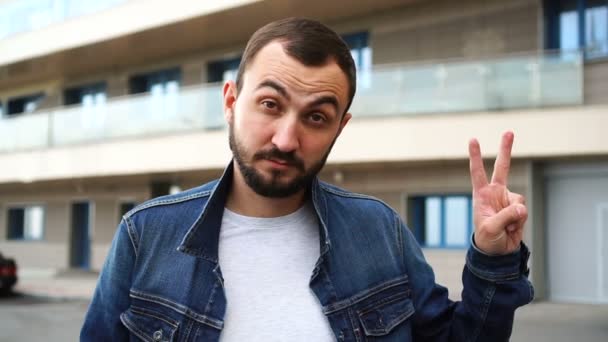 Красивый молодой человек с бородой показывает победный жест на улице — стоковое видео