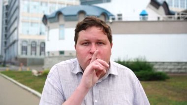 Sessizlik jesti yapan yakışıklı gülümseyen genç adam portresi. Kameraya bakan duygusal erkekler