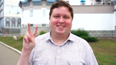 Zafer işareti gösteren yakışıklı gülümseyen genç adam portre. Kameraya bakan duygusal erkekler