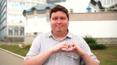 Yakışıklı gülümseyen genç adam portre aşk jesti gösteren. Kameraya bakan duygusal erkekler