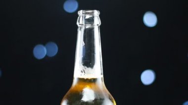 Açık bir şişede soğuk bira parlak ışıklar ile siyah bir arka plan üzerinde dönen