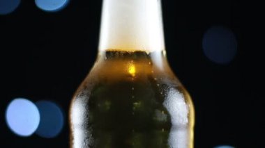 Parlak ışıklar ile siyah bir arka plan üzerinde dönen net bir şişe soğuk bira
