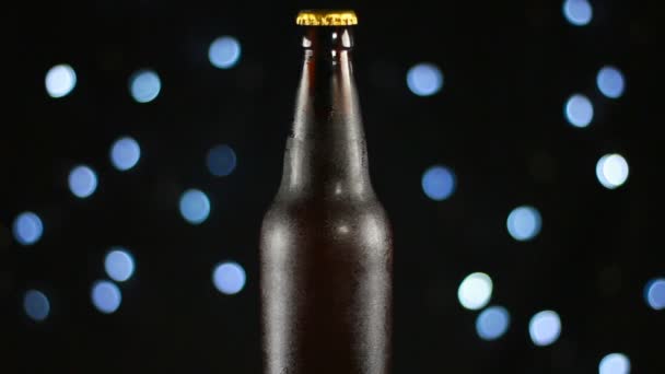 Cerveza oscura en una botella transparente girando sobre un fondo negro con luces brillantes — Vídeos de Stock