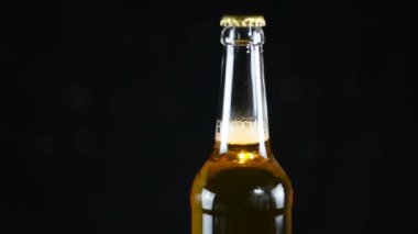 Kapalı bira şişesi siyah bir arka plan üzerinde dönen. Bir şişe biranın boynu metal bir kapakla kaplıdır.