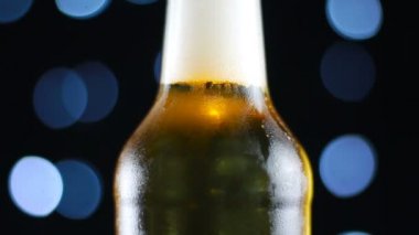 Parlak ışıklar ile siyah bir arka plan üzerinde dönen net bir şişe soğuk bira