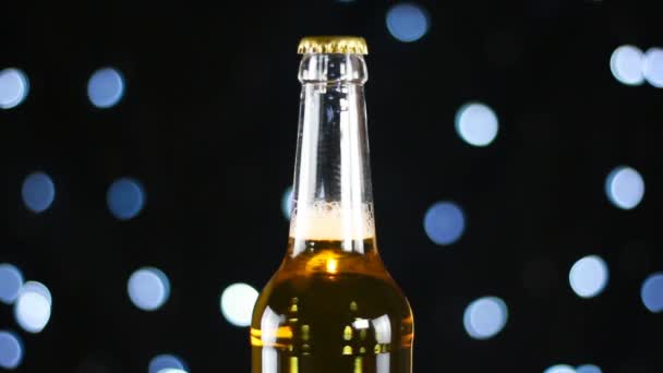 Cerveza fría en una botella transparente girando sobre un fondo negro con luces brillantes — Vídeos de Stock