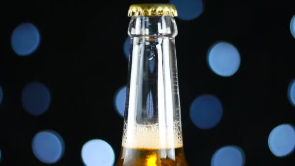 Cerveza de cerveza pálida en una botella transparente girando sobre un fondo negro con luces brillantes — Vídeos de Stock