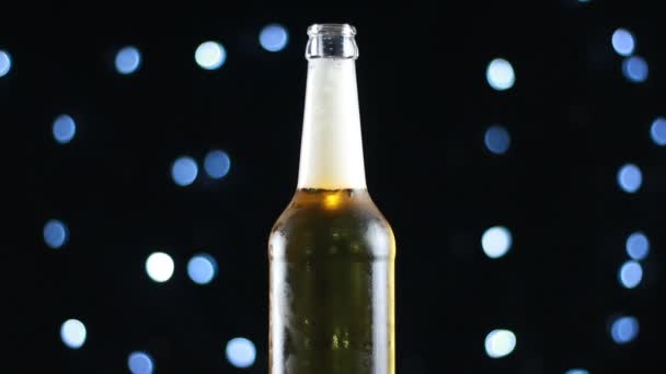 Cerveza en botella abierta girando sobre fondo negro con luces brillantes — Vídeos de Stock