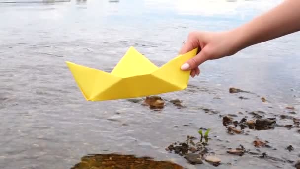 Womans hand innehar gult papper båt över floden — Stockvideo