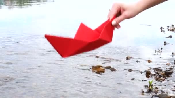 Womans hand holding red paper boat over the river and playing with him — Stock Video