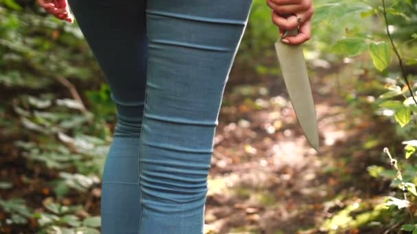 Una mujer con un cuchillo en la mano atraviesa un bosque verde y aterrador. Contenido protector o delictivo . — Vídeos de Stock