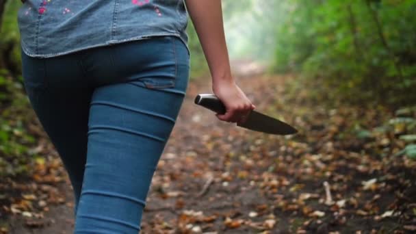 Yeşil ormanda yürüyen ve elinde bıçak olan genç bir kadın. Tehlike duygusu. — Stok video