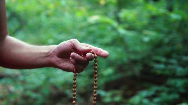 Gebetsperlen in der Hand. männliche Hand hält Rosenkranz, betet zu Gott auf grünem Naturhintergrund, religiöse Spiritualität. — Stockvideo