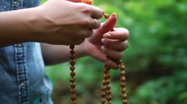 Elinde dua boncukları. Kadın el tespih tutan, yeşil doğa arka plan, dini maneviyat tanrıya dua.