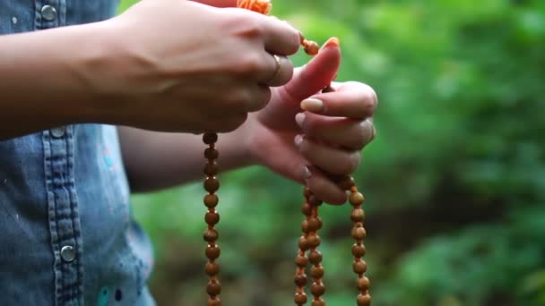 Bön pärlor i handen. Kvinnlig hand hålla Rosenkransen, be till Gud på grön natur bakgrund, religiös andlighet. — Stockvideo