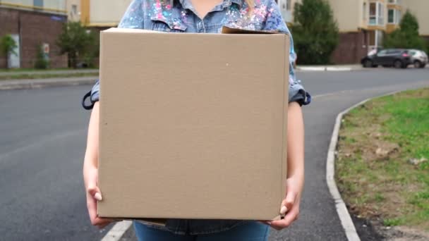 Mujer joven llevando una caja de cartón y caminando al aire libre — Vídeos de Stock