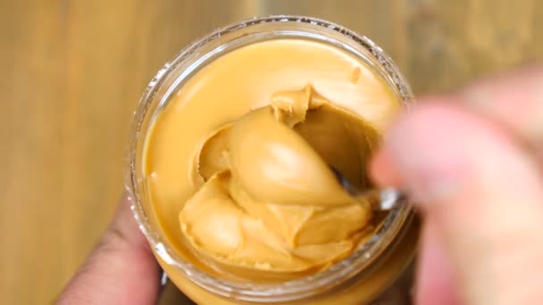 Mixing with a Spoon peanut butter. Creamy smooth peanut butter in jar backdrop — Stock Video