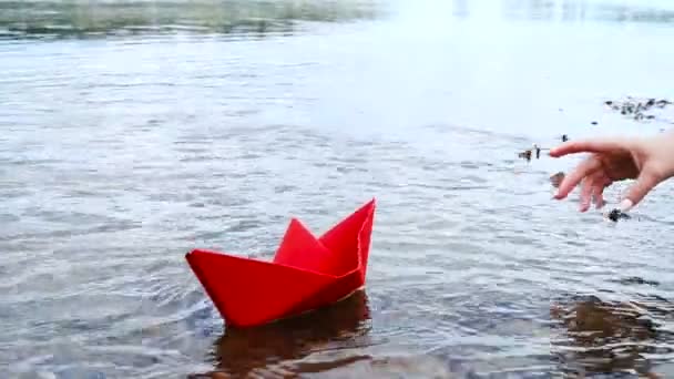 Frauenhand legt rotes Papierboot aufs Wasser und schiebt es weg — Stockvideo