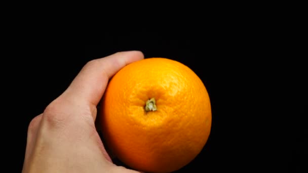 Man hand houdt een oranje citrus op een zwarte achtergrond — Stockvideo