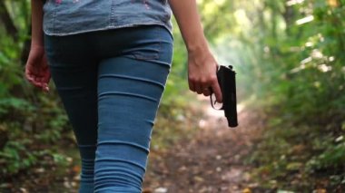 Yeşil, korkunç ormanda yürüyen ve elinde silah tutan bir kadın. Tehlike hissi. Koruyucu veya suçlu içeriği.