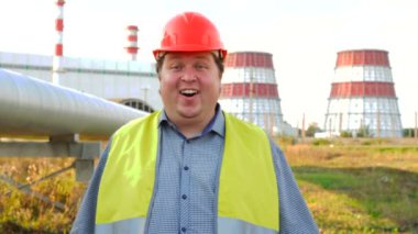 Elektrik santralinin önündeki kameraya bakan şaşkın işçi, mühendis ya da elektrikçi.