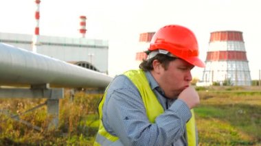 İşçi, mühendis ya da elektrikçi doğrudan kameraya bakıp elektrik santralinin önünde öksürüyor.