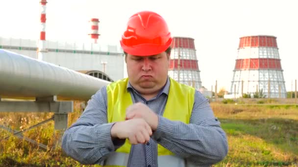 Pracownik, inżynier lub elektryk patrzący na pracownika kamery pokazuje jak pracować stojąc przed elektrownią — Wideo stockowe