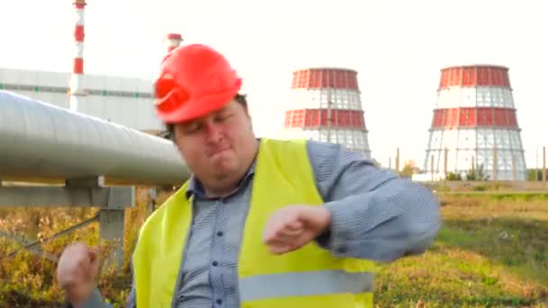 Pracownik, inżynier lub elektryk patrzący bezpośrednio w kamerę tańczącą przed elektrownią — Wideo stockowe