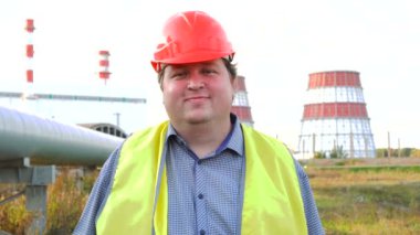Mutlu işçi, mühendis ya da elektrikçi doğrudan kameraya bakıyor ve elektrik santralinin önünde gülümsüyor.